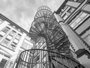 looking up at a spiral fire escape with sky above - black and white