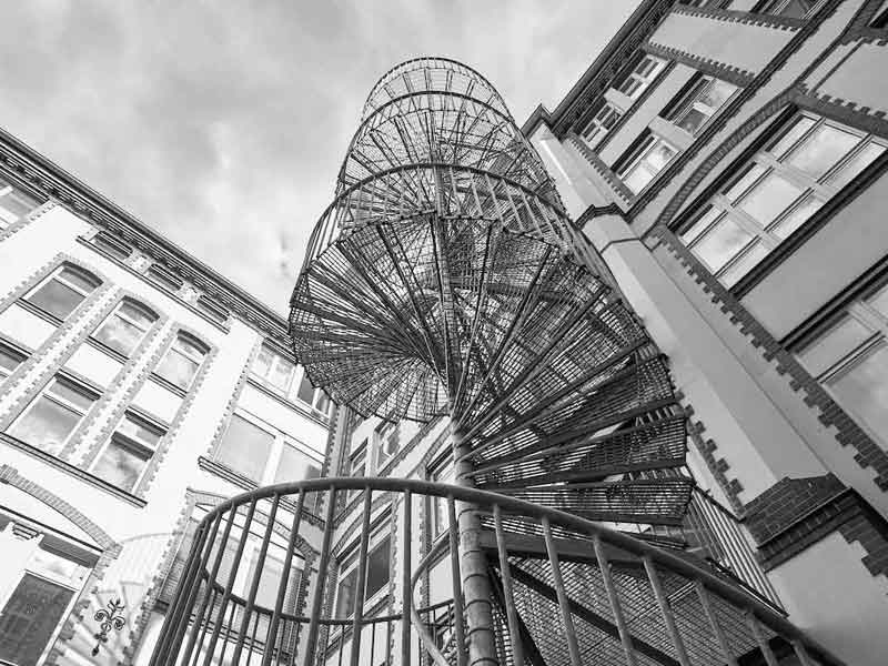 looking up at a spiral fire escape with sky above - black and white
