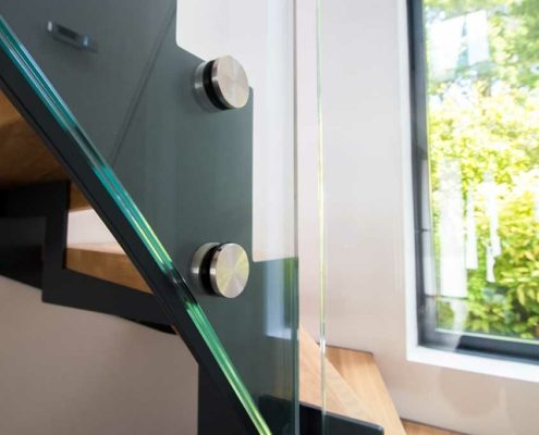close up of side of stair showing steel stringer, glass and stainless clamps with window behind