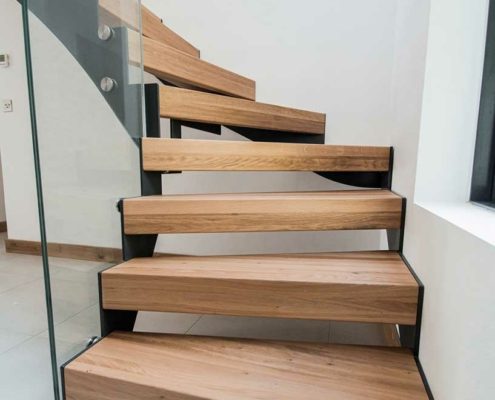 bottom section of a modern oak and glass stair with tiled floor below