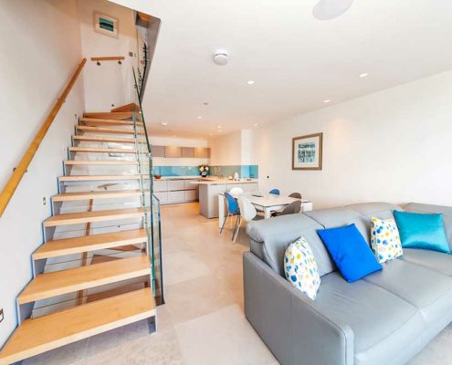 living room with sofa in foreground, modern stair on left and kitchen to rear