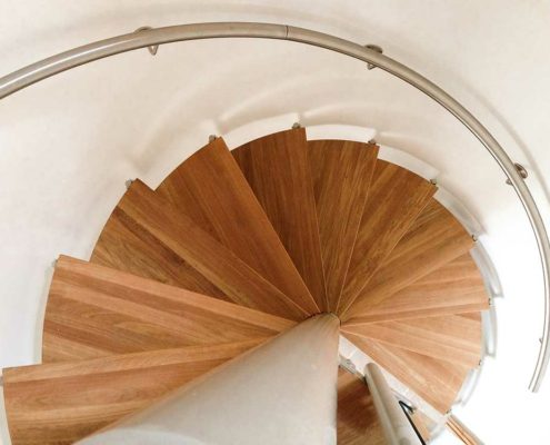 looking down on a spiral stair with oak steps and a wall mounted stainless handrail