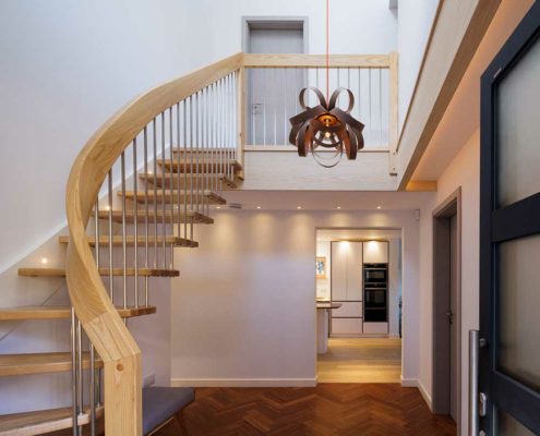 Floating stair in a hallway with a light feature light hanging down. Kitchen in background