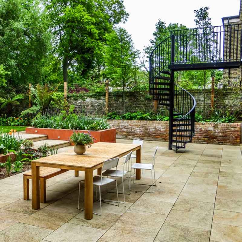 outdoor wooden table on patio with spiral behind and green trees